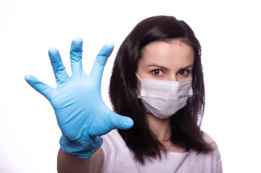 Yüzünde tıbbi maske, ellerinde eldivenler olan genç bir kadın.