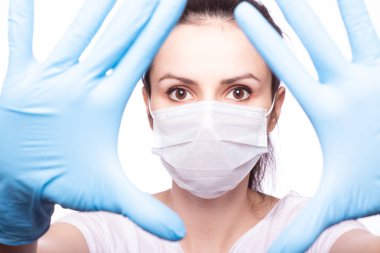 Yüzünde tıbbi maske, ellerinde eldivenler olan genç bir kadın.