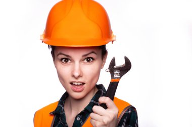 Güzel genç kız miğferli işçi elinde bir İngiliz anahtarı tutuyor.