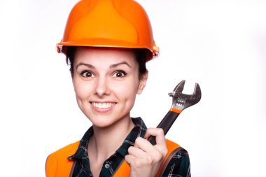 Güzel genç kız miğferli işçi elinde bir İngiliz anahtarı tutuyor.