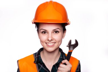 Güzel genç kız miğferli işçi elinde bir İngiliz anahtarı tutuyor.