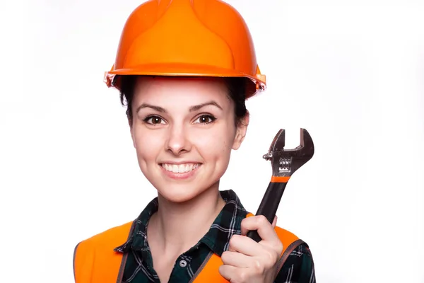 beautiful young girl worker in a helmet holds in her hand a wrench