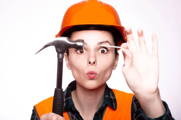 建設用ヘルメットの美しい少女労働者は手にハンマーと釘を持っています — ストック写真