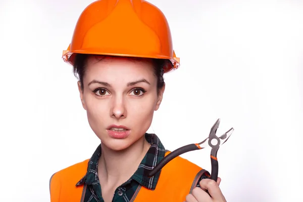 beautiful young girl worker in a helmet holds pliers in her hand