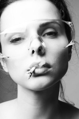 Güvenlik gözlüklü güzel bir kız ağzında sigara, siyah beyaz bir fotoğraf.