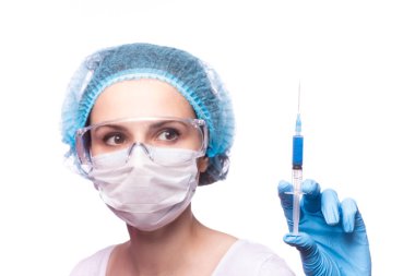 Tıp maskeli, gözlüklü ve eldivenli genç bir kız elinde mavi sıvı bir şırınga tutuyor.