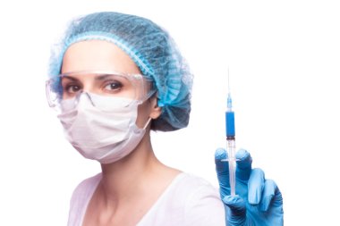 Tıp maskeli, gözlüklü ve eldivenli genç bir kız elinde mavi sıvı bir şırınga tutuyor.