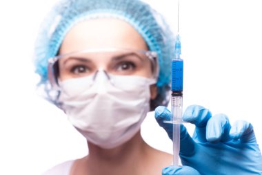 Tıp maskeli, gözlüklü ve eldivenli genç bir kız elinde mavi sıvı bir şırınga tutuyor.