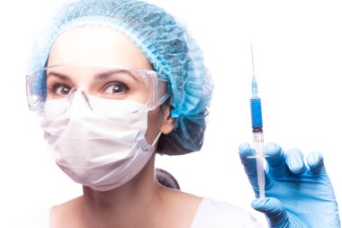 Tıp maskeli, gözlüklü ve eldivenli genç bir kız elinde mavi sıvı bir şırınga tutuyor.