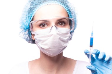 Tıp maskeli, gözlüklü ve eldivenli genç bir kız elinde mavi sıvı bir şırınga tutuyor.