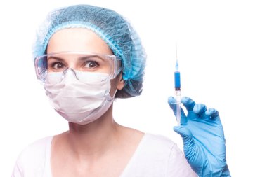 Tıp maskeli, gözlüklü ve eldivenli genç bir kız elinde mavi sıvı bir şırınga tutuyor.