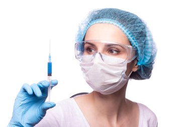 Tıp maskeli, gözlüklü ve eldivenli genç bir kız elinde mavi sıvı bir şırınga tutuyor.