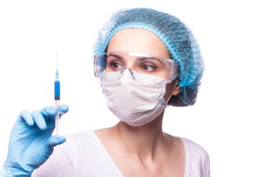 Tıp maskeli, gözlüklü ve eldivenli genç bir kız elinde mavi sıvı bir şırınga tutuyor.