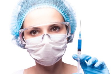 Tıp maskeli, gözlüklü ve eldivenli genç bir kız elinde mavi sıvı bir şırınga tutuyor.