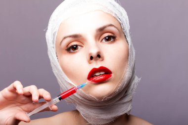 Güzel genç bir kız, dudakları kırmızı rujla boyanmış, kafası bandajlı, elinde kırmızı bir sıvıyla bir şırınganın
