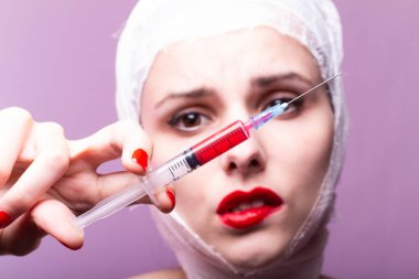 Güzel genç bir kız, dudakları kırmızı rujla boyanmış, kafası bandajlı, elinde kırmızı bir sıvıyla bir şırınganın