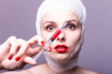 Güzel genç bir kız, dudakları kırmızı rujla boyanmış, kafası bandajlı, elinde kırmızı bir sıvıyla bir şırınganın