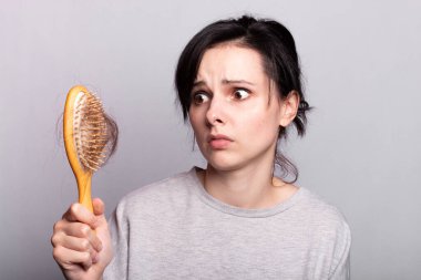 Saç dökülmesi, bir kadın tarağa bakar, uygun saç bakımına değil.