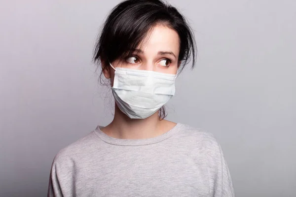 woman with bangs in a gray sweater and medical mask on her face, coronavirus pandemic