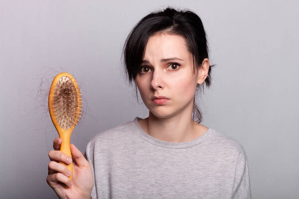 эмоциональная девушка держит расческу в руках с пучком выпадения волос
