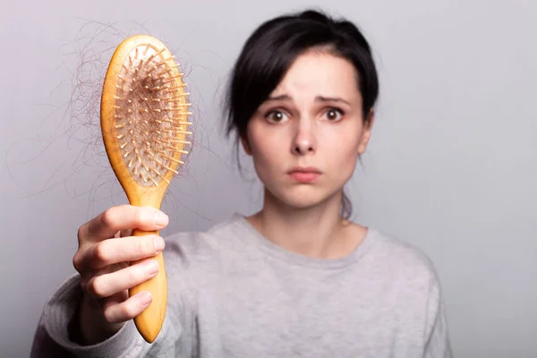 emotional girl holding a comb in her hands with a bundle of hair loss