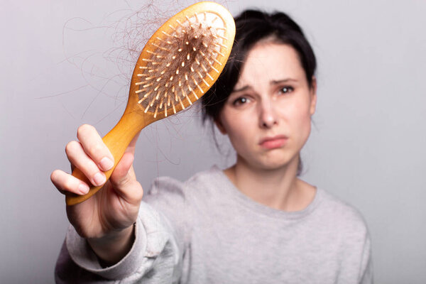 эмоциональная девушка держит расческу в руках с пучком выпадения волос
