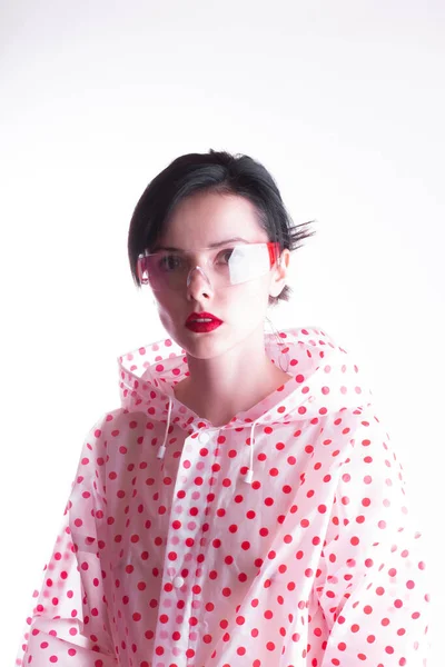 woman in a raincoat with red polka dots, transparent safety glasses, strange fashionable style