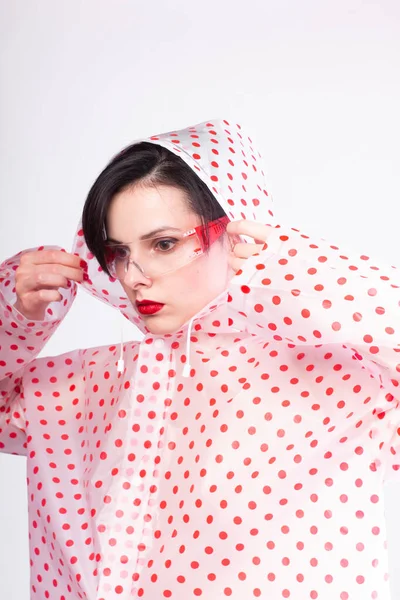 woman in a raincoat with red polka dots, transparent safety glasses, red lips
