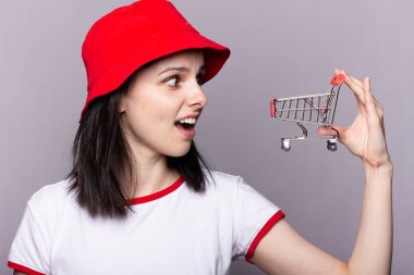 Kırmızı panama şapkalı güzel bir kadın alışveriş arabasıyla markete gidiyor.