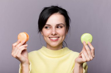 Genç esmer Rus kadın izole edilmiş arka planda elinde renkli Fransız kurabiyeleri ve mutlu bir ifadeyle.