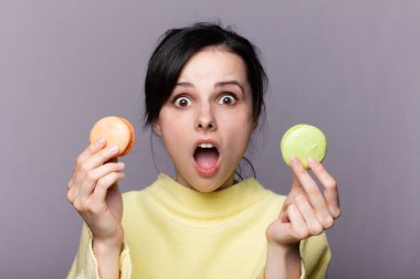 Genç esmer Rus kadın izole edilmiş arka planda elinde renkli Fransız kurabiyeleri ve mutlu bir ifadeyle.