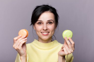 Genç esmer Rus kadın izole edilmiş arka planda elinde renkli Fransız kurabiyeleri ve mutlu bir ifadeyle.