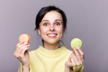 Genç esmer Rus kadın izole edilmiş arka planda elinde renkli Fransız kurabiyeleri ve mutlu bir ifadeyle.