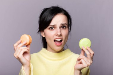 Çekici bir kadının profili kapalıyken lezzetli, pembe bir makaronu ısırmak, elinde kurabiye, güzel bir moda kızı yemekten, diyet konseptinden, abur cuburdan, kilo kaybından zevk alıyor.