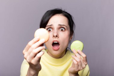 Çekici bir kadının profili kapalıyken lezzetli, pembe bir makaronu ısırmak, elinde kurabiye, güzel bir moda kızı yemekten, diyet konseptinden, abur cuburdan, kilo kaybından zevk alıyor.