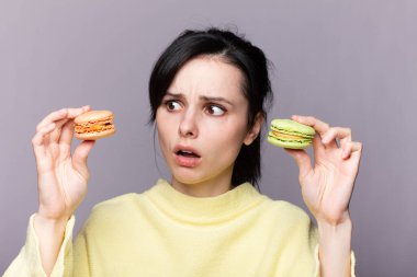 Çekici bir kadının profili kapalıyken lezzetli, pembe bir makaronu ısırmak, elinde kurabiye, güzel bir moda kızı yemekten, diyet konseptinden, abur cuburdan, kilo kaybından zevk alıyor.