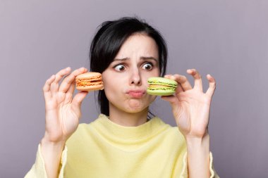 Çekici bir kadının profili kapalıyken lezzetli, pembe bir makaronu ısırmak, elinde kurabiye, güzel bir moda kızı yemekten, diyet konseptinden, abur cuburdan, kilo kaybından zevk alıyor.