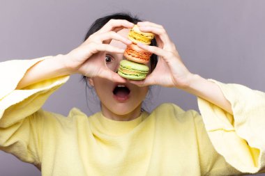 Çekici bir kadının profili kapalıyken lezzetli, pembe bir makaronu ısırmak, elinde kurabiye, güzel bir moda kızı yemekten, diyet konseptinden, abur cuburdan, kilo kaybından zevk alıyor.