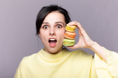 Çekici bir kadının profili kapalıyken lezzetli, pembe bir makaronu ısırmak, elinde kurabiye, güzel bir moda kızı yemekten, diyet konseptinden, abur cuburdan, kilo kaybından zevk alıyor.