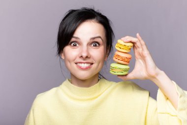 Çekici bir kadının profili kapalıyken lezzetli, pembe bir makaronu ısırmak, elinde kurabiye, güzel bir moda kızı yemekten, diyet konseptinden, abur cuburdan, kilo kaybından zevk alıyor.