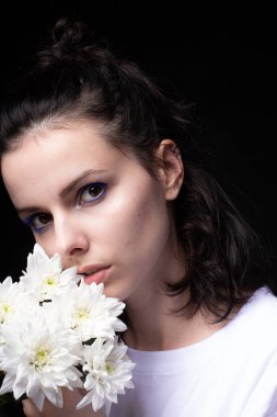 Elinde kasımpatı tutan sıra dışı mavi makyajlı bir kadın. Siyah stüdyo geçmişi var.