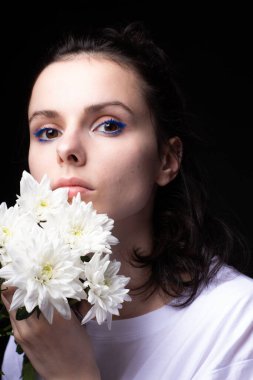 Elinde kasımpatı tutan sıra dışı mavi makyajlı bir kadın. Siyah stüdyo geçmişi var.