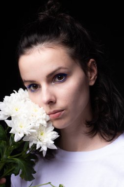 Elinde kasımpatı tutan sıra dışı mavi makyajlı bir kadın. Siyah stüdyo geçmişi var.