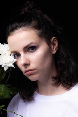 Elinde kasımpatı tutan sıra dışı mavi makyajlı bir kadın. Siyah stüdyo geçmişi var.