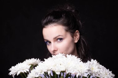 Büyük bir buket kasımpatı ve siyah arkaplanı olan güzel bir kadın.