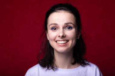 Kırmızı arka planda hafif tişörtlü gülümseyen kadın.