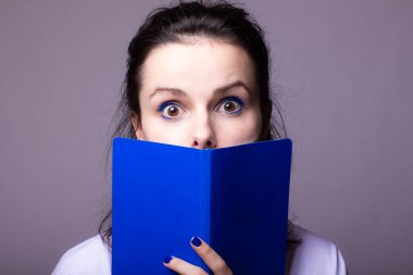 Elinde mavi not defteri olan duygusal bir kadın, gri stüdyo geçmişi var.