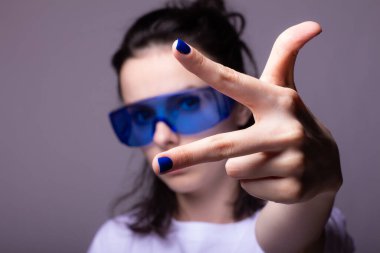 Büyük mavi gözlüklü, gri arka planlı komik kız.