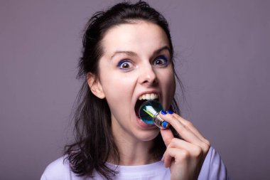 Ağzında ampul tutan kadın, gri arka plan.