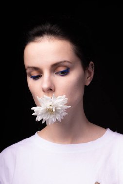 Ağzında beyaz kasımpatı tutan bir kadın, siyah arka plan.